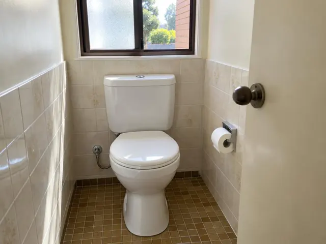 Clean white toilet in a tiled bathroom with a window and toilet roll holder in Meadowbank