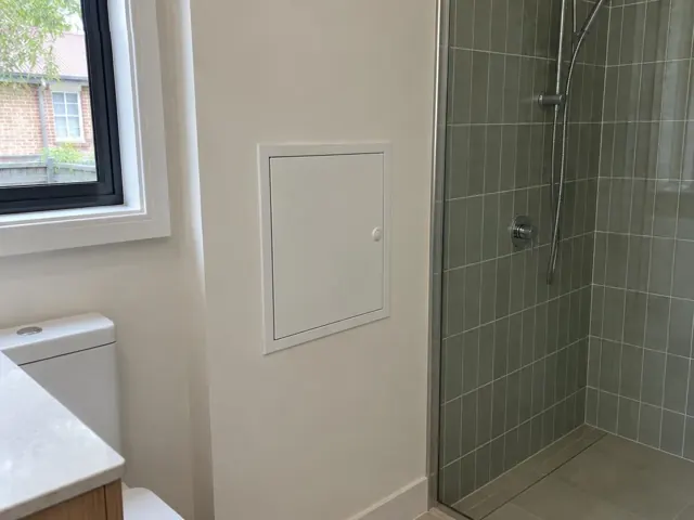 Small access panel in a bathroom wall beside a tiled shower in Mortlake